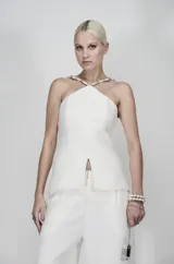 Blusa blanca estructurada en tweed con diseño halter y detalle metálico bordado en el cuello. Presenta una abertura frontal sutil y corte entallado en la cintura.