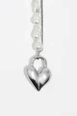 Collar de doble cadena, una compuesta por perlas barrocas y otra de eslabones metálicos finos, unidas por un dije central en forma de corazón plateado con cierre tipo barra.