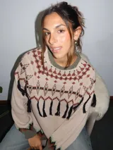 Sweater tejido con técnica intarsia, de silueta holgada y cuello a la base. Presenta un diseño con motivos geométricos, detalles de flecos colgantes y terminaciones en tejido acanalado en color rojo en puños y ruedo.