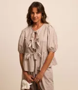 Blusa Marfinno confeccionada en tricolina de algodón con estampado de cuadros vichy, de manga corta abullonada, cuello redondo, abertura frontal con lazos y recorte fruncido en la cintura.