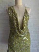 Vestido corto ajustado color verde lima, con escote pronunciado en V tipo drapeado y tirantes finos. El vestido está cubierto de lentejuelas plateadas.