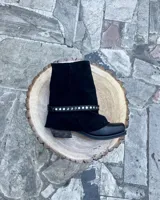 Botas de cuero vacuno color negro, con diseño versátil que incluye una polaina desmontable y un estribo decorativo con tachas metálicas. Presentan un taco bajo y punta redondeada.