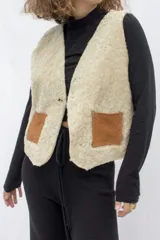 Chaleco reversible confeccionado en cuero genuino. Presenta un lado de piel de oveja gris con bolsillos de cuero negro y un lado de cuero liso gris. Diseño sin mangas con cierre frontal.
