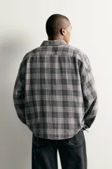 Camisa de algodón con corte boxy fit, diseño a cuadros en tonos grises y blancos, cuello clásico y manga larga con puños abotonados.