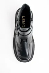 Bota corta de cuero negro con suela track dentada y dos correas decorativas con hebillas metálicas en el lateral. Presenta un diseño de puntera cuadrada y cierre lateral.