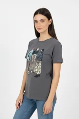 Remera de algodón color gris oscuro, con cuello redondo a la base y mangas cortas. Presenta un estampado frontal artístico con detalles en glitter que ilustra a tres figuras femeninas.