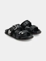 Sandalia de cuero negro de estilo boho con dos tiras anchas, hebillas grandes metálicas y herrajes plateados, con base cómoda.