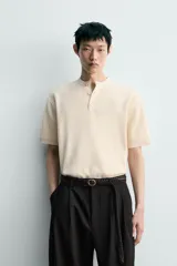 Camiseta regular fit de punto tejido en hilatura de algodón de color beige, con cuello redondo y cierre frontal de botonadura tipo panadero, manga corta y acabados en rib.