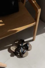 Sandalias bajas de cuero color beige con doble tira de cuero negro con textura y hebilla metálica.