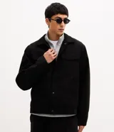 Campera tipo trucker de gamuza sintética color negro, con cuello clásico, bolsillos delanteros con solapa y cierre frontal por botones metálicos.