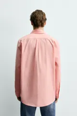 Camisa de corte relajado color celeste, confeccionada en mezcla de algodón y seda. Presenta cuello solapa, cierre frontal de botones, manga larga con puños abotonados y dos bolsillos de plastrón con solapa en el pecho.