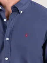 Camisa lisa de hombre confeccionada en algodón, tintada en prenda con acabado vintage. Presenta corte regular fit, cuello buttondown, cierre frontal de botones, manga larga con puño simple y logo bordado en el pecho.