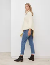 Poncho tejido color crema, con cuello polera y diseño trenzado diagonal en el frente. Presenta un corte asimétrico en el ruedo.