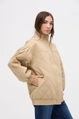 Campera bomber de gabardina con diseño capitoneado, cuello alto, cierre frontal con botones a presión ocultos y mangas abullonadas con puños elásticos.
