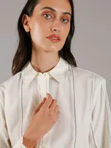 Camisa de popelín de algodón color blanco con finas rayas verticales negras, de corte regular, manga larga, cuello en punta, cierre de botones y bajo redondeado.