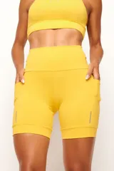 Short biker deportivo de tiro alto, color amarillo, con bolsillos laterales funcionales y detalles reflectivos en el ruedo. Cuenta con cintura anatómica y bolsillo interno 360° en la cintura.