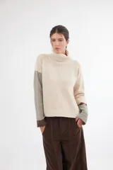 Polera de calce relajado con cuello alto, confeccionada en lana. Presenta un diseño bicolor con cuerpo en gris claro y mangas con estampado jacquard de arabescos en tonos tierra y negro. Incluye detalle de costura central vertical en el frente.