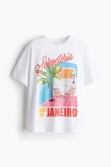 Remera blanca de algodón con cuello redondo y hombros caídos, con un estampado gráfico que muestra una escena de playa o terraza con una palmera, sillas de lona a cuadros y el texto "Sorveteria Rio de Janeiro".