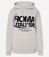 Buzo oversized color beige con capucha ajustable y bolsillo canguro. Presenta un estampado frontal estilo college con el texto "ROMA ITALY 1987" en negro y detalles en azul. Tiene puños y bajo ajustados.