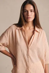 Camisa oversize de manga corta, color rosado con finas rayas verticales oscuras, cuello camisero y cierre frontal de botones.