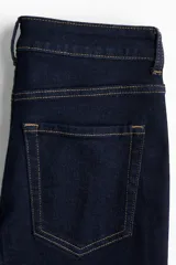 Jeans de cinco bolsillos en denim índigo oscuro, tiro alto, corte ajustado en la parte superior y pierna acampanada (flare) desde la rodilla. Presenta costuras en hilo contrastante color caramelo.