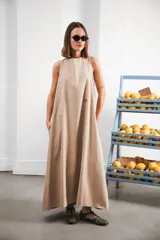 Vestido largo color beige, de corte amplio y cómodo, con escote a la base, espalda con leve abertura, bolsillos laterales y logo bordado a contratono en el frente.