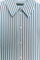 Camisa de corte oversize con estampado de rayas verticales en tonos celeste y negro. Presenta cuello solapa, cierre frontal con botones y mangas largas con puños rectos.