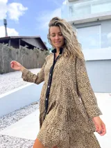 Vestido camisero de corte holgado y diseño escalonado, con estampado animal print en tonos beige y negro. Presenta cuello camisero, cierre frontal con botones y mangas largas con puños.