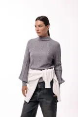 Polera de tejido de punto color marrón, con cuello alto y diseño de trenzas verticales. Presenta mangas largas con puños ajustados y un detalle de panel lateral asimétrico que se anuda en la cintura.