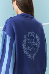 Cardigan de algodón color azul con mangas largas de rayas verticales anchas en tonos azul y celeste, puños en rojo, y bordado en la espalda con diseño de escudo nacional.
