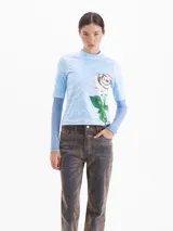 Top de cuello alto con mangas cortas, confeccionado en tejido de punto con estampado de efecto cielo y una rosa grande en el frente. Presenta un diseño entallado al cuerpo.