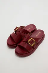 Sandalias planas de eco cuero color bordó, con tiras cruzadas y hebilla metálica dorada.