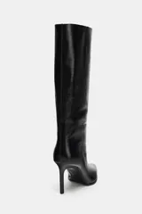 Bota de caña alta y ancha confeccionada en piel, con diseño de punta fina y tacón alto tipo aguja. Presenta costuras decorativas a lo largo del cuerpo y un diseño de calce fácil.