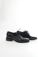 Zapato de charol negro de cuero vacuno con textura grabada tipo reptil, punta cuadrada y cordones al tono.