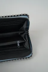 Billetera rectangular color celeste claro, con borde decorado con tachas metálicas plateadas y cierre de cremallera plateado en el lateral.