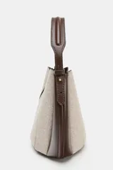 Bolso tipo saca con diseño estructurado, confeccionado en una combinación de tejido de lana en tono beige y laterales de cuero sintético marrón. Presenta costuras decorativas verticales, asa de mano superior y una correa bandolera extraíble con detalle de franjas. Cuenta con cierre mediante botón imantado.