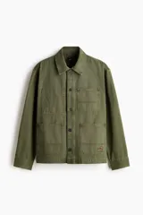 Sobrecamisa de lona de algodón en color verde militar, con cuello clásico, cierre frontal de botones y tres bolsillos de parche frontales. Presenta mangas largas con puños abotonados y un diseño de corte recto.