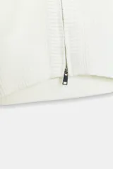 Chaqueta de punto color blanco con cuello subido, cierre frontal de cremallera metálica y mangas largas abullonadas con puños ajustados.