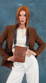 Phonebag pequeña color mostaza, confeccionada en cuero sintético, con solapa frontal y correa ajustable con logo de la marca.