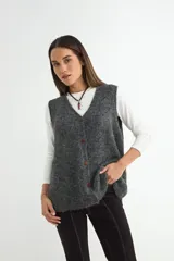 Chaleco tejido de punto en color gris oscuro, con escote en V y cierre frontal de botones marrones. Presenta una textura suave y un corte holgado.