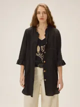 Camisa de lino y algodón de silueta relajada, largo irregular y color negro. Cuenta con mangas con volados, cuello mao con detalle fruncido y cierre frontal con botones a contratono.