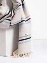 Bufanda de tejido suave en color marrón chocolate con diseño de rayas horizontales en tonos naranja, beige y gris. Presenta terminaciones con flecos en los extremos.