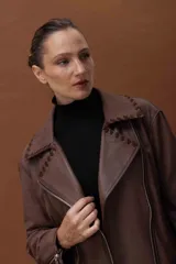 Chaqueta estilo motoquera de cuero ovino color marrón, con diseño oversize. Presenta detalles artesanales de pasamanería en cuello, solapas y bolsillos, cierre frontal cruzado y cierres metálicos en los puños.