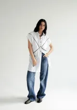 Vestido camisero corto blanco de algodón con bordados negros, cuello camisero, cierre frontal con botones y sin mangas.