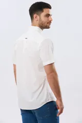 Camisa lisa de algodón azul marino, de manga corta, con cuello camisero, cierre frontal de botones y un bolsillo aplicado en el pecho.