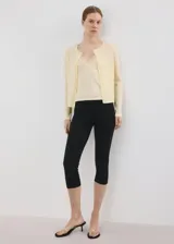 Chaleco de punto fino color amarillo claro, de corte recto, con cuello redondo, manga larga y cierre delantero de botonadura completa.