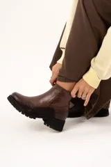 Bota de cuero color chocolate con caña al tobillo y cierre lateral. Presenta una combinación de texturas en el cuero y una suela chunky dentada de color negro.