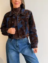 Campera corta de denim con diseño marmolado en tonos azul y marrón, de corte clásico con cierre frontal de botones metálicos y bolsillos en el pecho.