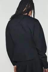 Chaqueta de cuello redondo y manga larga con pliegues, de color negro, con falsos bolsillos de vivo en el delantero y cierre frontal con botones.