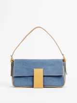 Cartera tipo bandolera de jean azul con ribetes y detalles de cuero tostado, asa de hombro y solapa frontal con cierre magnético y trabilla central.